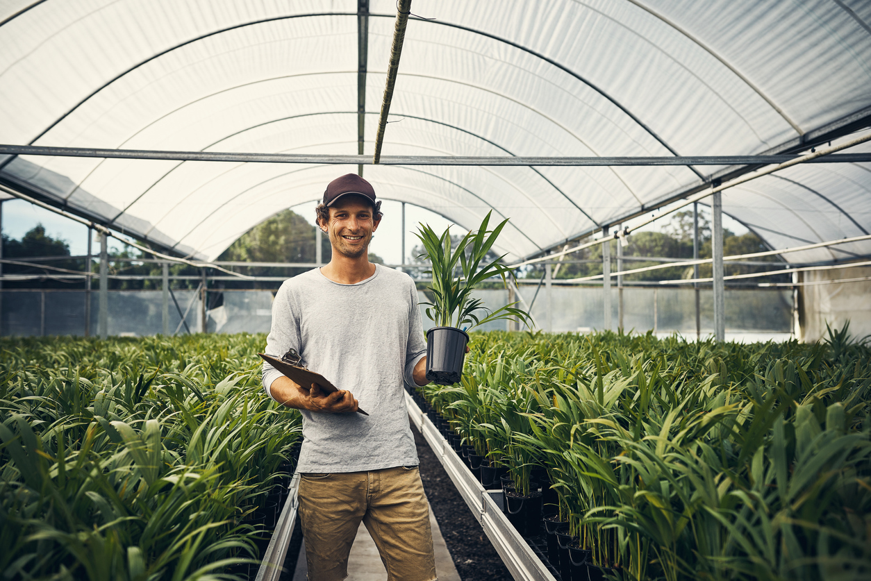 Farmer standing in a greenhouse holding a potted plant and clipboard
